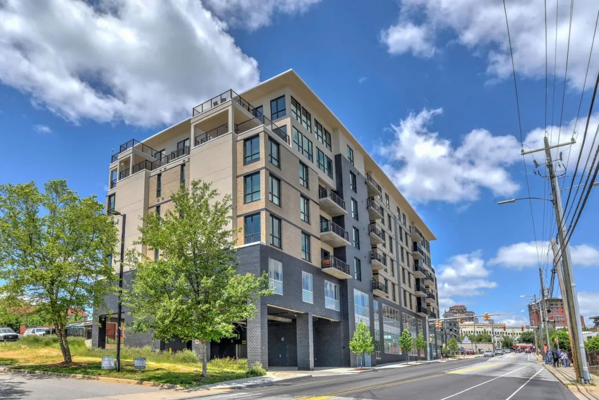 The modern exterior of the condominium, featuring spacious balconies and expansive windows overlooking greenery and the vibrant neighborhood. The balconies are designed for enjoying sunset views and outdoor relaxation above the city streets.