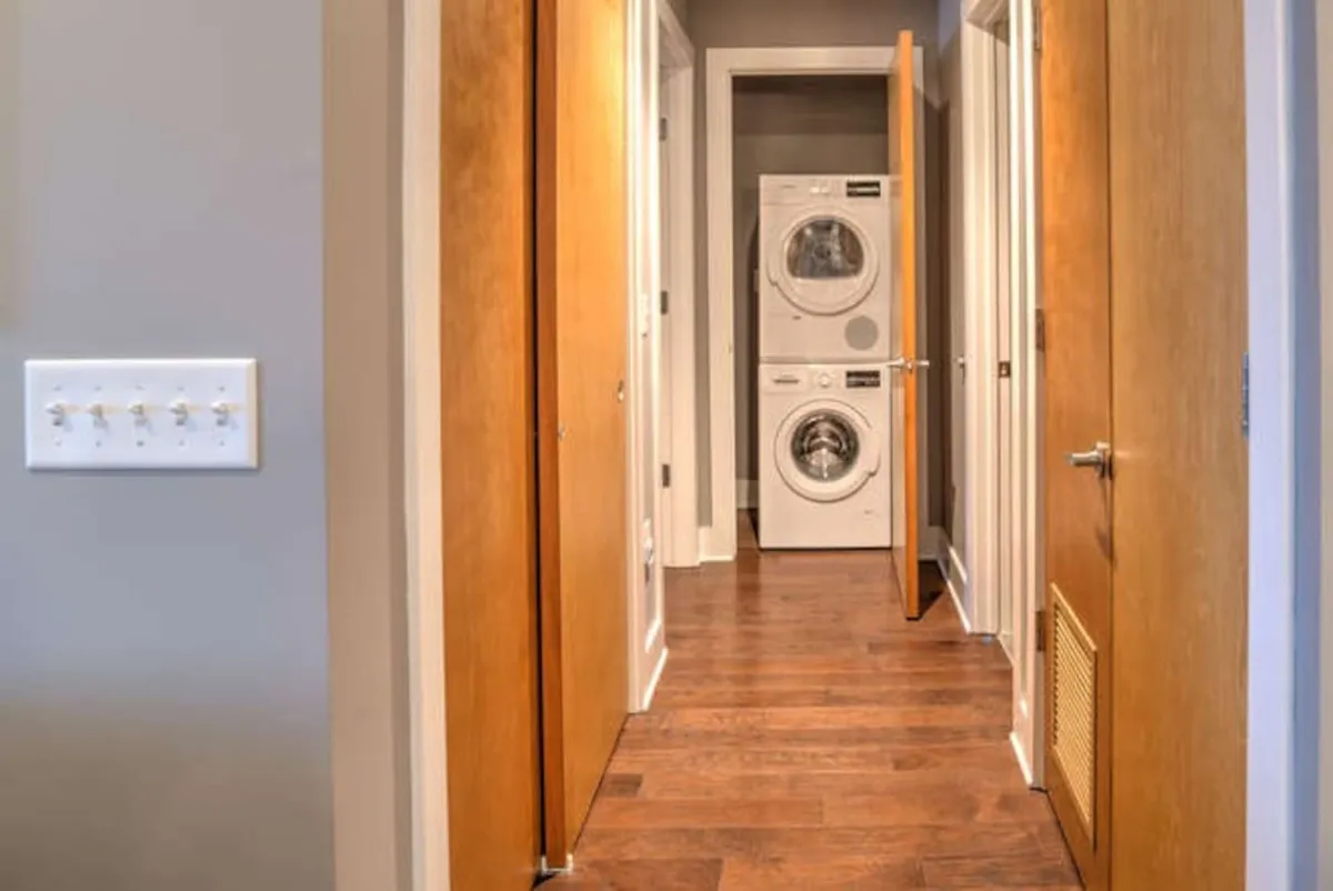 This image depicts a functional interior utility space featuring a washing machine and dryer, wooden doors, and a light switch. The area appears tidy, organized, and practical, emphasizing the ease of daily living and modern conveniences available within the property.