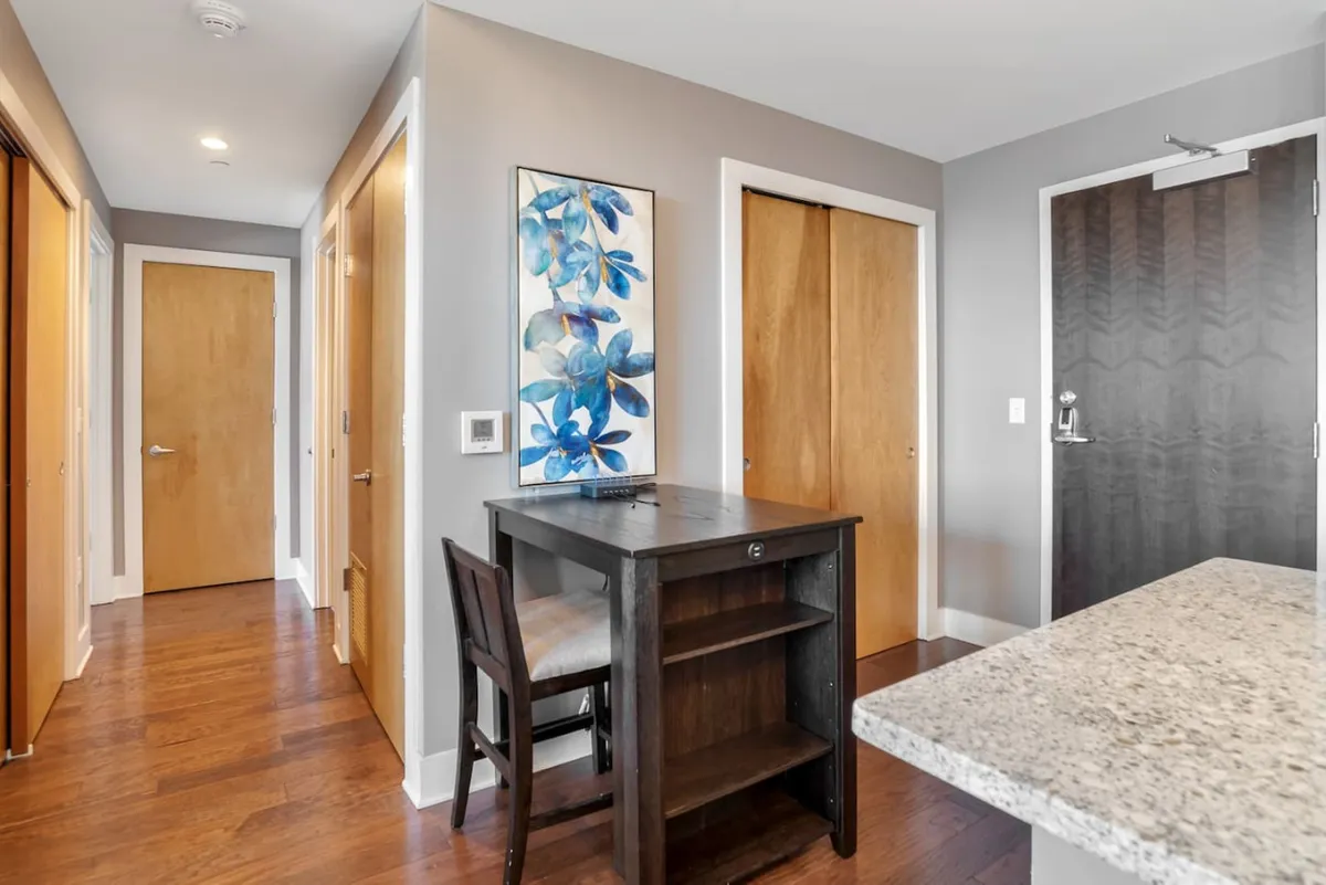 A calm, inviting entry area with a small desk, tasteful artwork, and wooden doors. The layout suggests a welcoming lobby or foyer, ideal for greeting guests or transitioning into the home from the secure entry point.